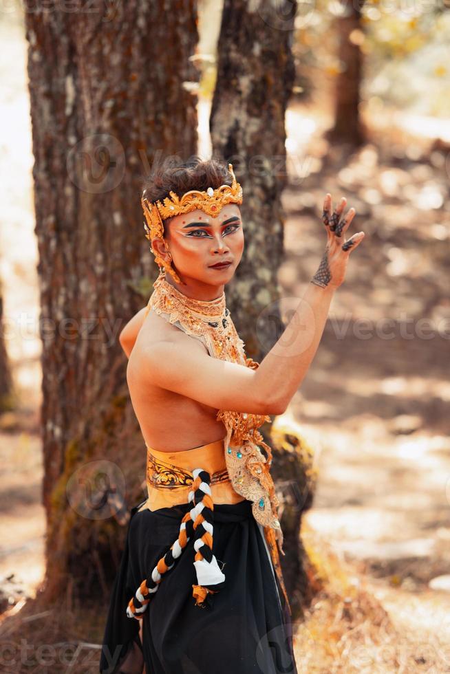 männlicher asiatischer mann, der in einer goldenen krone und in goldenen kleidern aufwirft, während er make-up trägt foto