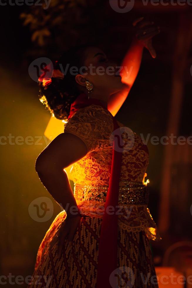 balinesische frauen, die kulturelle kleidung tragen, während sie mit tänzerischen bewegungen vor der beleuchtung posieren foto