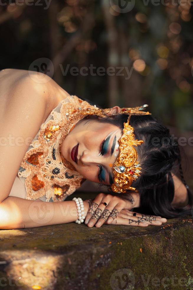 balinesische Frau mit goldener Krone und goldener Halskette, die auf dem Felsen schläft foto