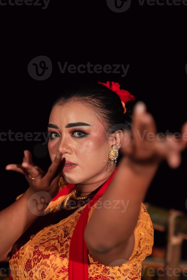 das wilde Gesicht einer balinesischen Frau mit Make-up in einem traditionellen orangefarbenen Kleid und einem roten Schal, während sie auf dem Festival tanzt foto