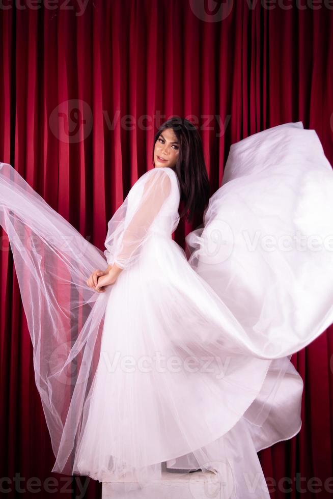 asiatische frau posiert in einem glamourösen hochzeitskleid mit fliegendem stoff aus dem kleid foto