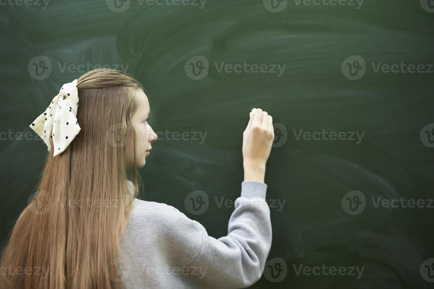 Ein junges Mädchen im Mittelschulalter schreibt mit Kreide auf eine Tafel. foto