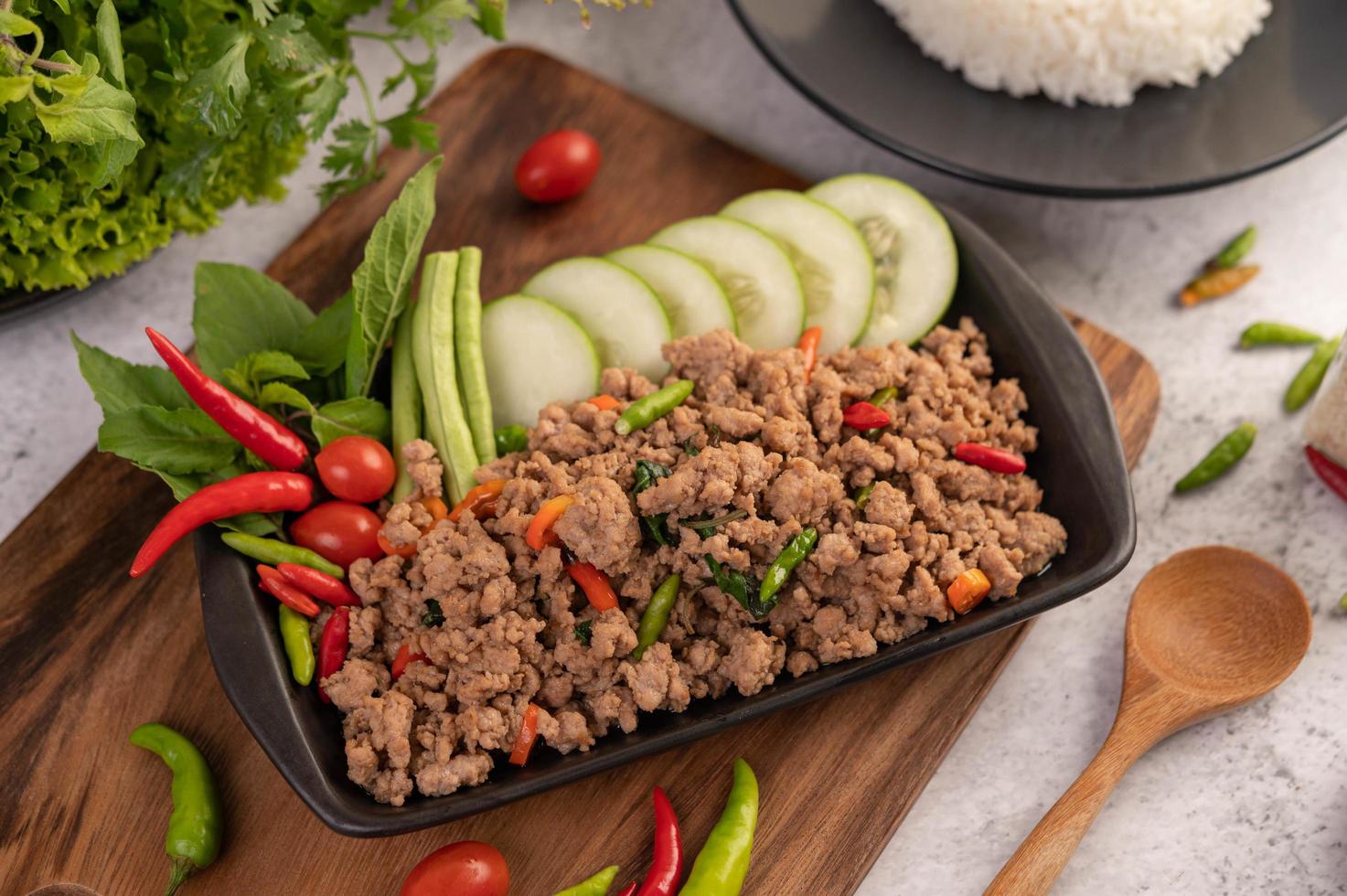 würziger gehackter Schweinefleischsalat mit Reis, Chili und Tomaten auf einem schwarzen Teller foto