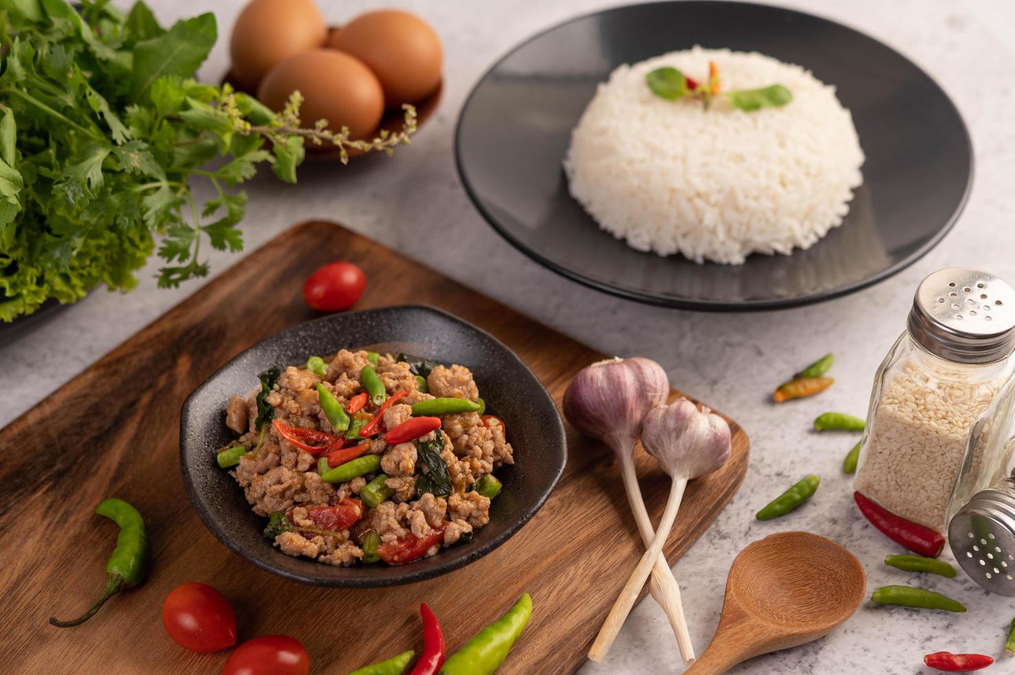 würziger gehackter Schweinefleischsalat mit Reis, Chili und Tomaten auf einem schwarzen Teller foto