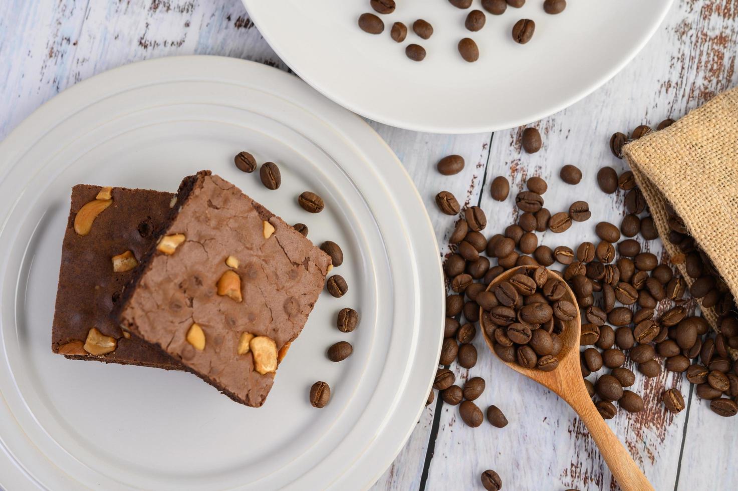 Schokoladen-Brownies auf einem weißen Teller und Kaffeebohnen auf einem Holzlöffel foto