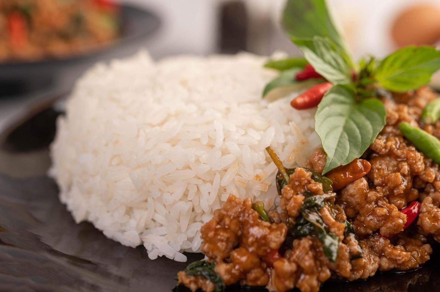 würziger gehackter Schweinefleischsalat mit Reis, Chili und Tomaten in einem schwarzen Teller foto