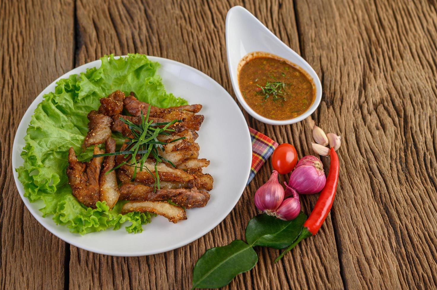 Schweinehals gegrillt auf einem weißen Teller mit roten Zwiebeln, Tomaten und Chili auf einem Holztisch foto