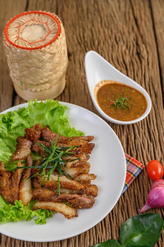 Schweinehals gegrillt auf einem weißen Teller mit roten Zwiebeln, Tomaten und Chili auf einem Holztisch foto