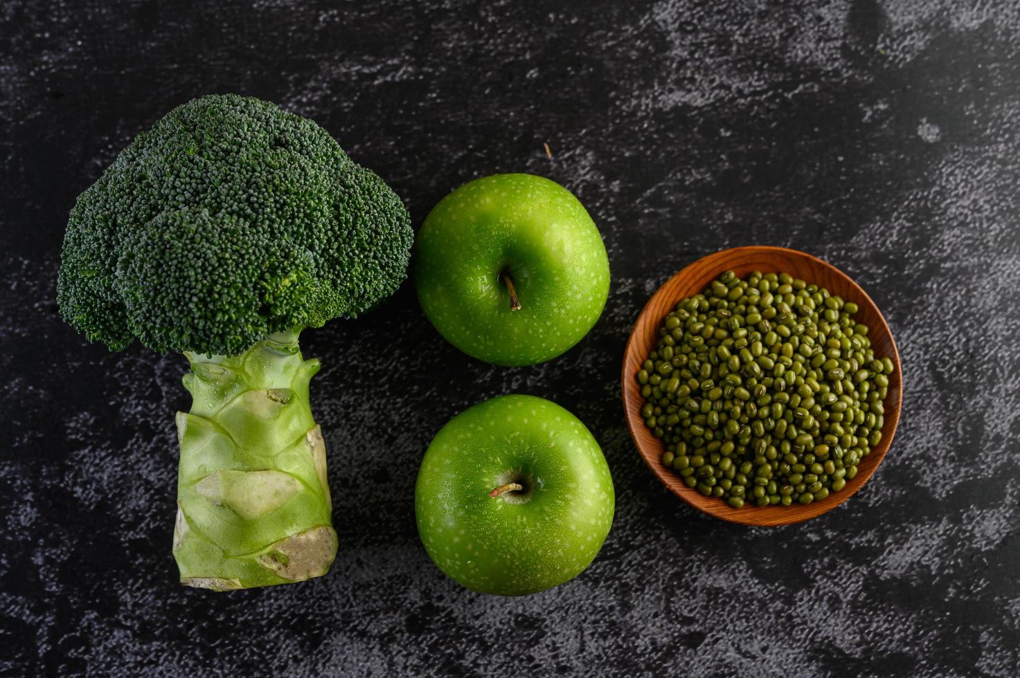 Brokkoli, Apfel und Mungobohne auf einem schwarzen Zementbodenhintergrund foto