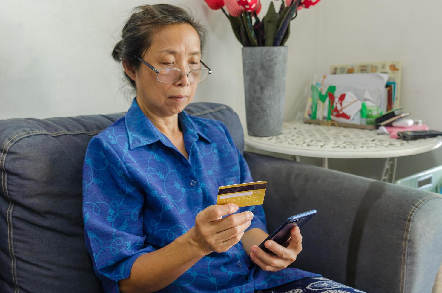 ältere asiatische Frau, die eine Kreditkarte benutzt, um online einzukaufen foto