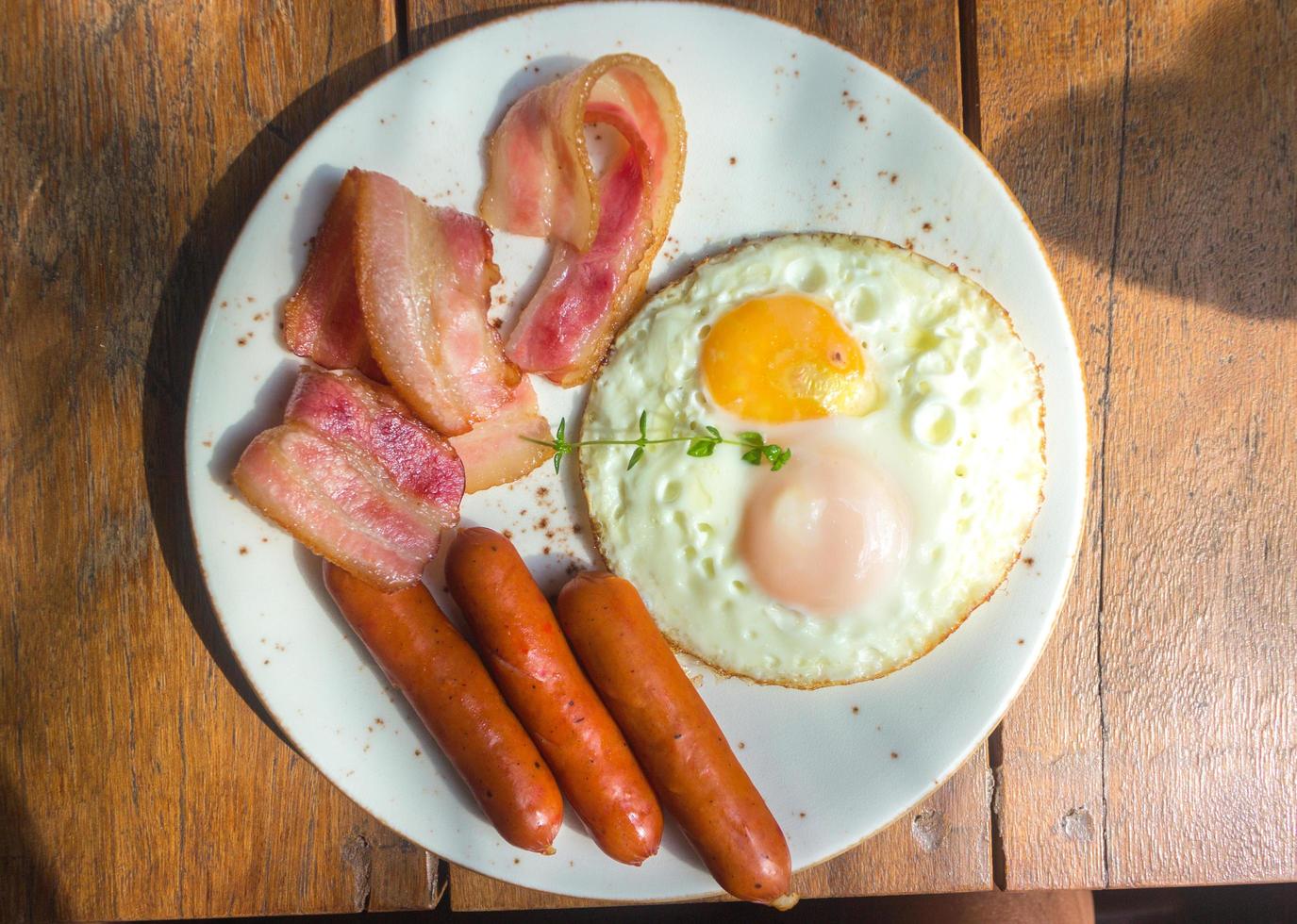 Speck, Spiegeleier und Wurst auf weißem Teller und Holztisch foto