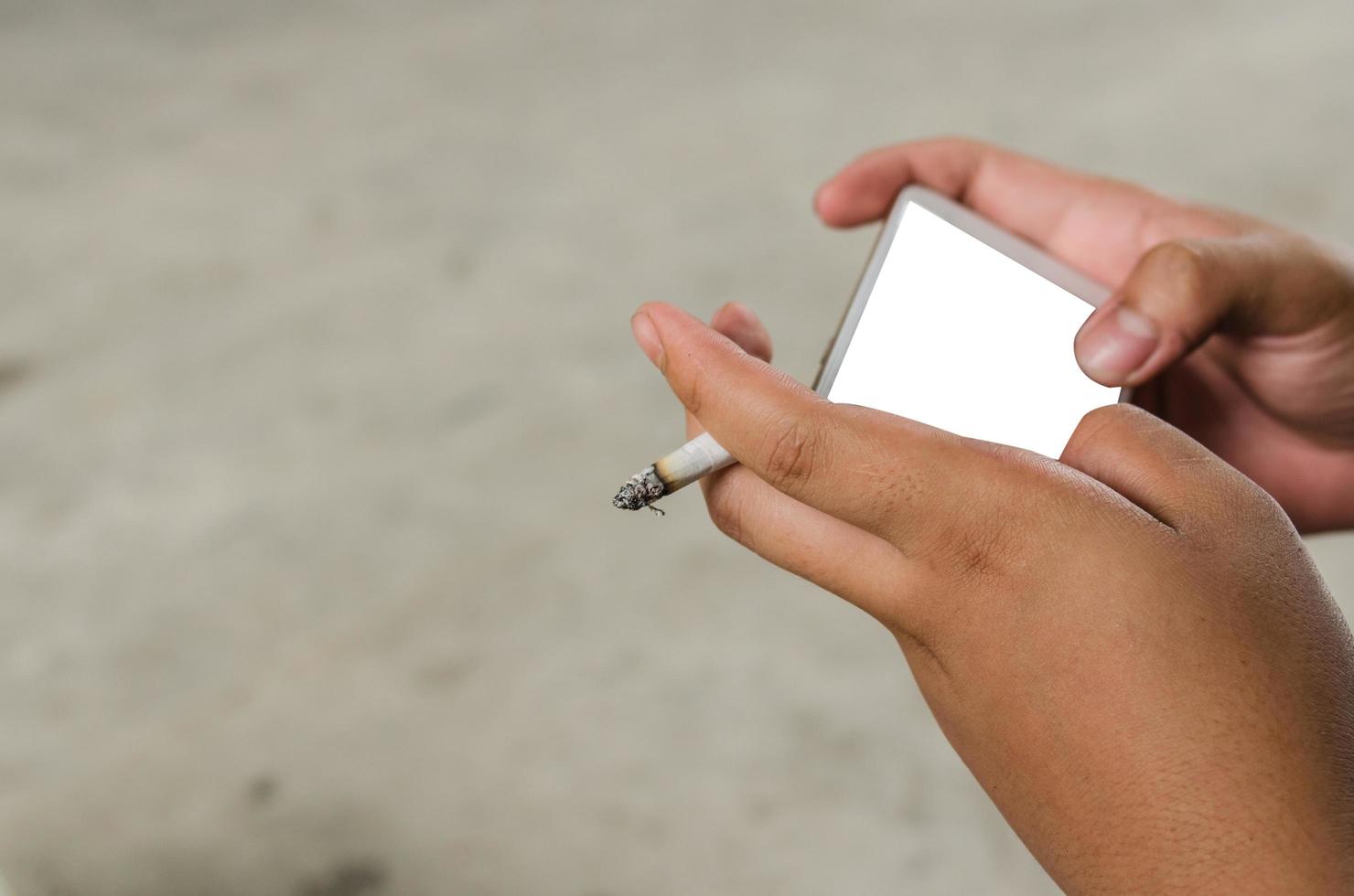 Person, die das Smartphone benutzt, während sie eine Zigarette raucht foto