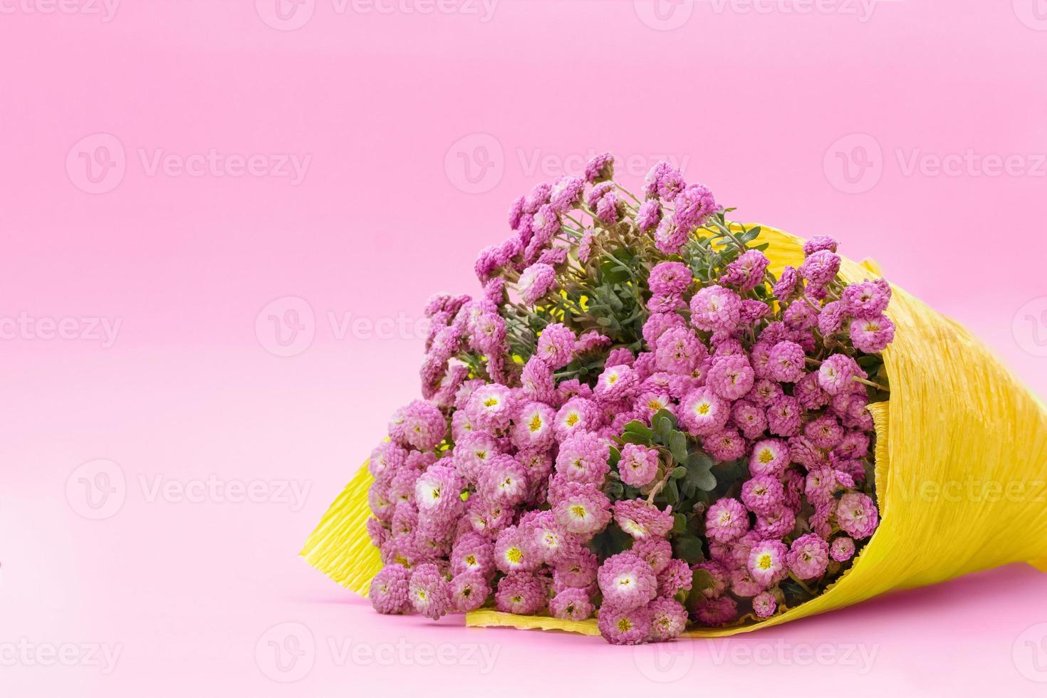 Blumenstrauß aus kleinen lila Chrysanthemen in gelbem Papier auf grünem Hintergrund. glückwunsch, geburtstagsgeschenk, internationaler frauentag, muttertag. Platz kopieren foto