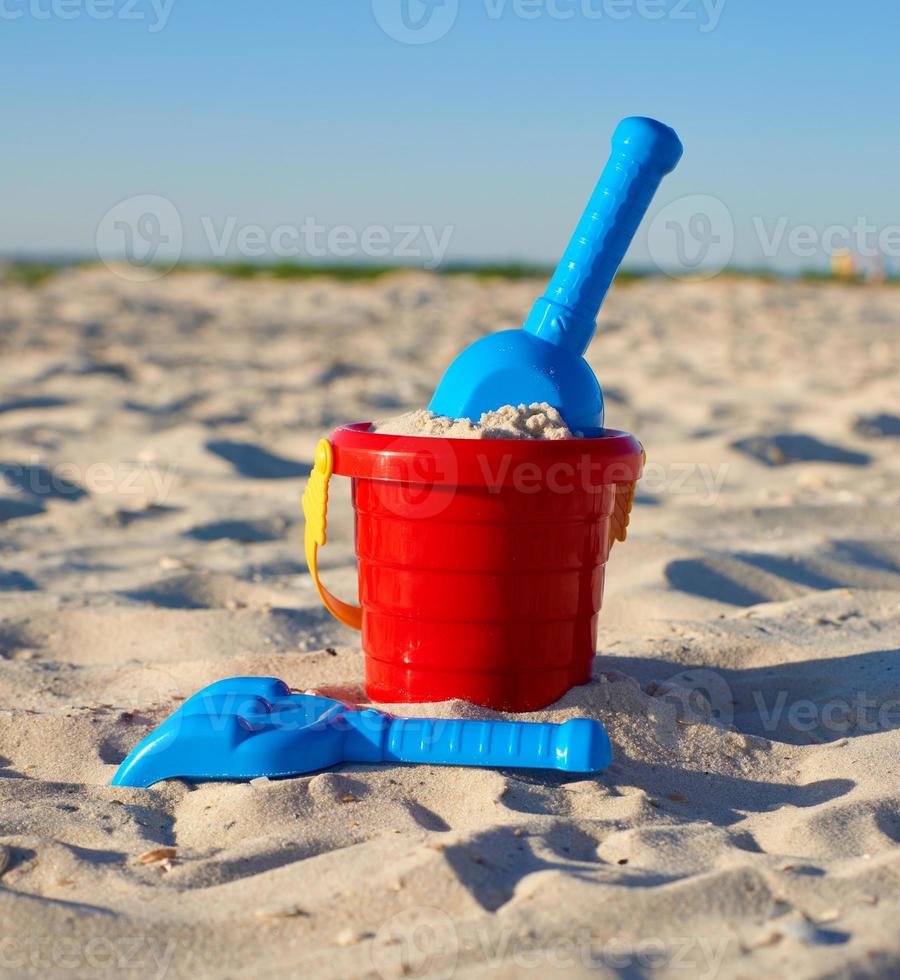 roter Plastikeimer und blauer Rechen, Schaufel auf dem Sand foto