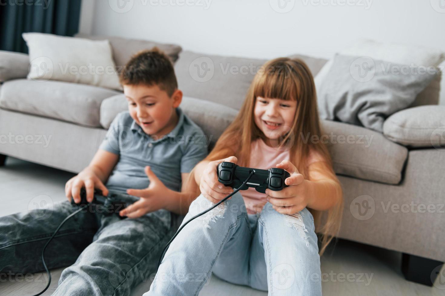 auf dem Boden sitzen und Videospiel spielen. Kinder, die sich tagsüber gemeinsam im Wohnzimmer amüsieren foto