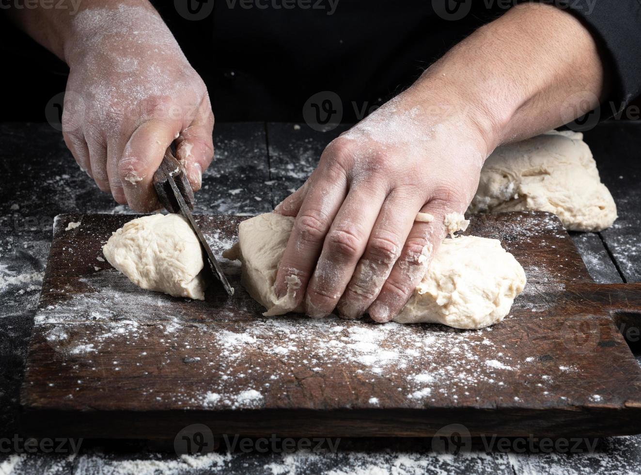 Küchenchef schneidet weißen Weizenmehlteig in Stücke foto