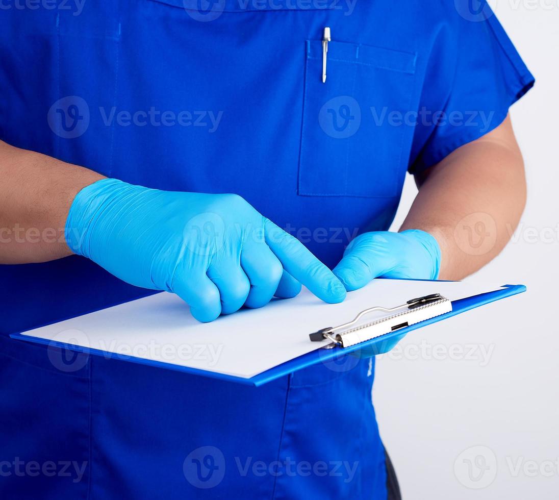 arzt in blauer uniform und latexhandschuhen hält einen blauen halter für papierblätter foto