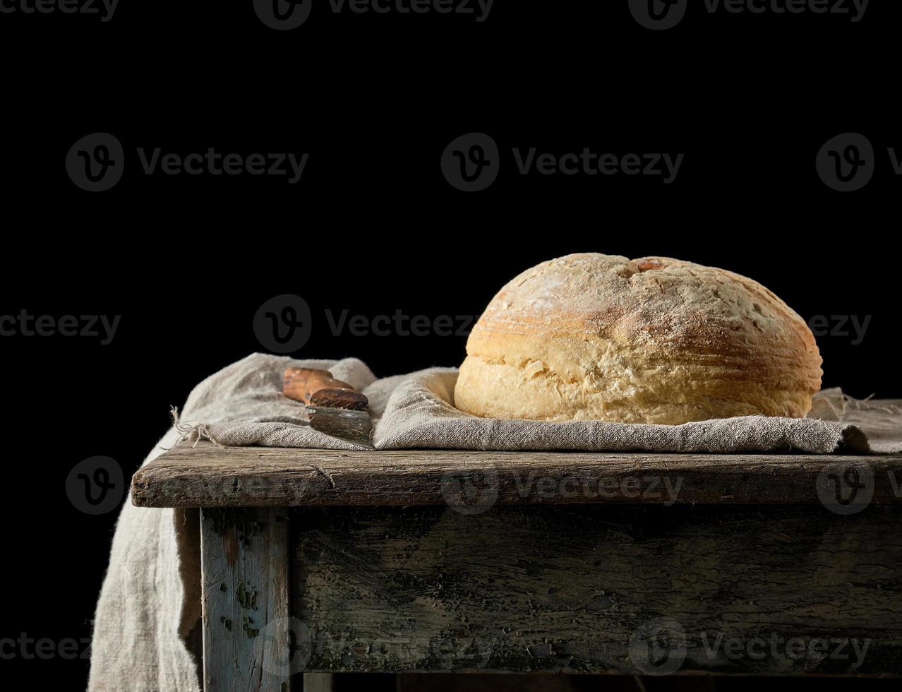 gebackenes rundes weißes Weizenbrot auf einem Textilhandtuch, alter Holztisch foto