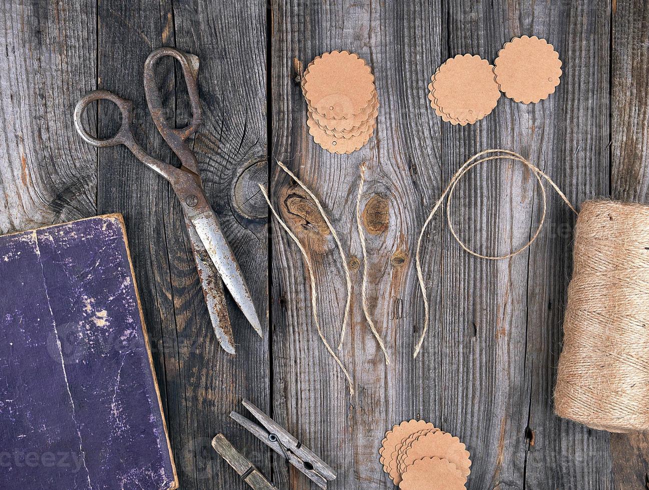 Spule aus braunem Seil, Papieretiketten und alten Scheren auf grauem Holzhintergrund foto