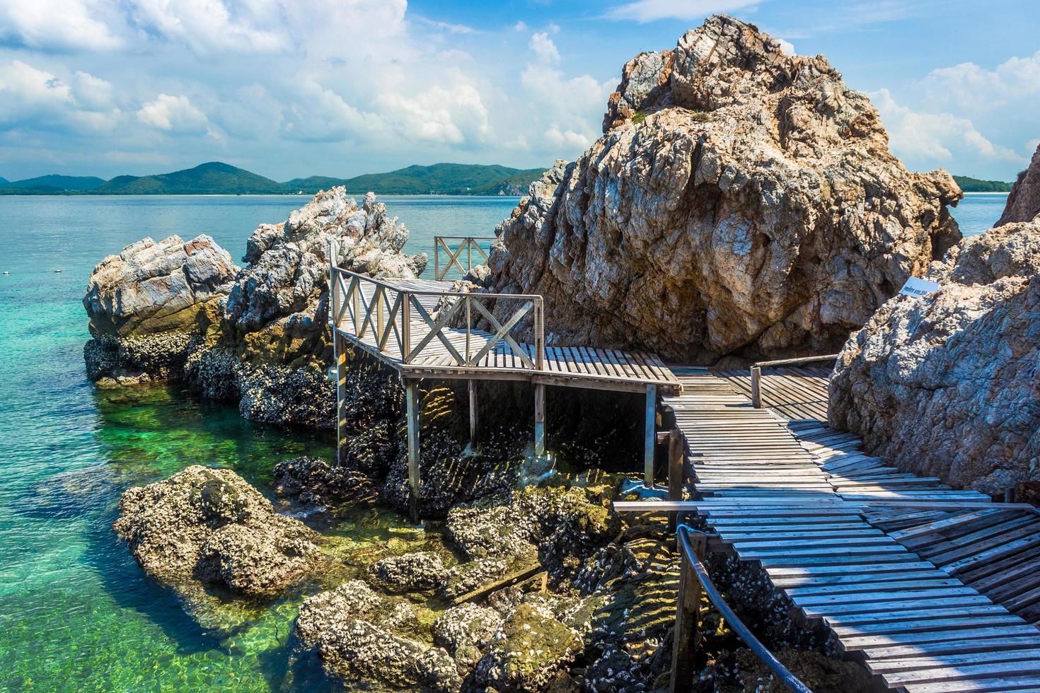 tropischer Inselfelsen und Holzbrücke am Strand mit bewölktem blauem Himmel foto