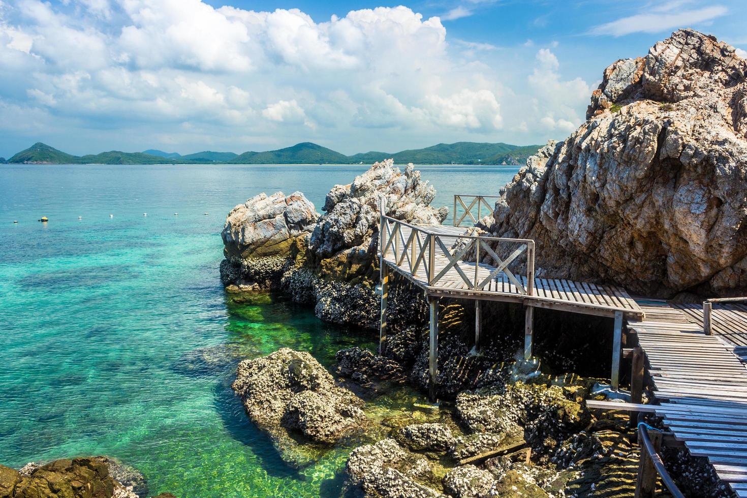 tropischer Inselfelsen und Holzbrücke am Strand mit bewölktem blauem Himmel foto