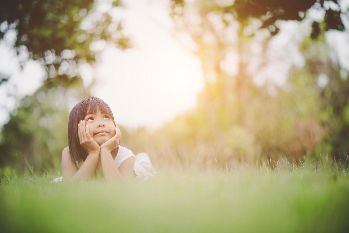 kleines Mädchen, das bequem auf Gras liegt und lächelt foto