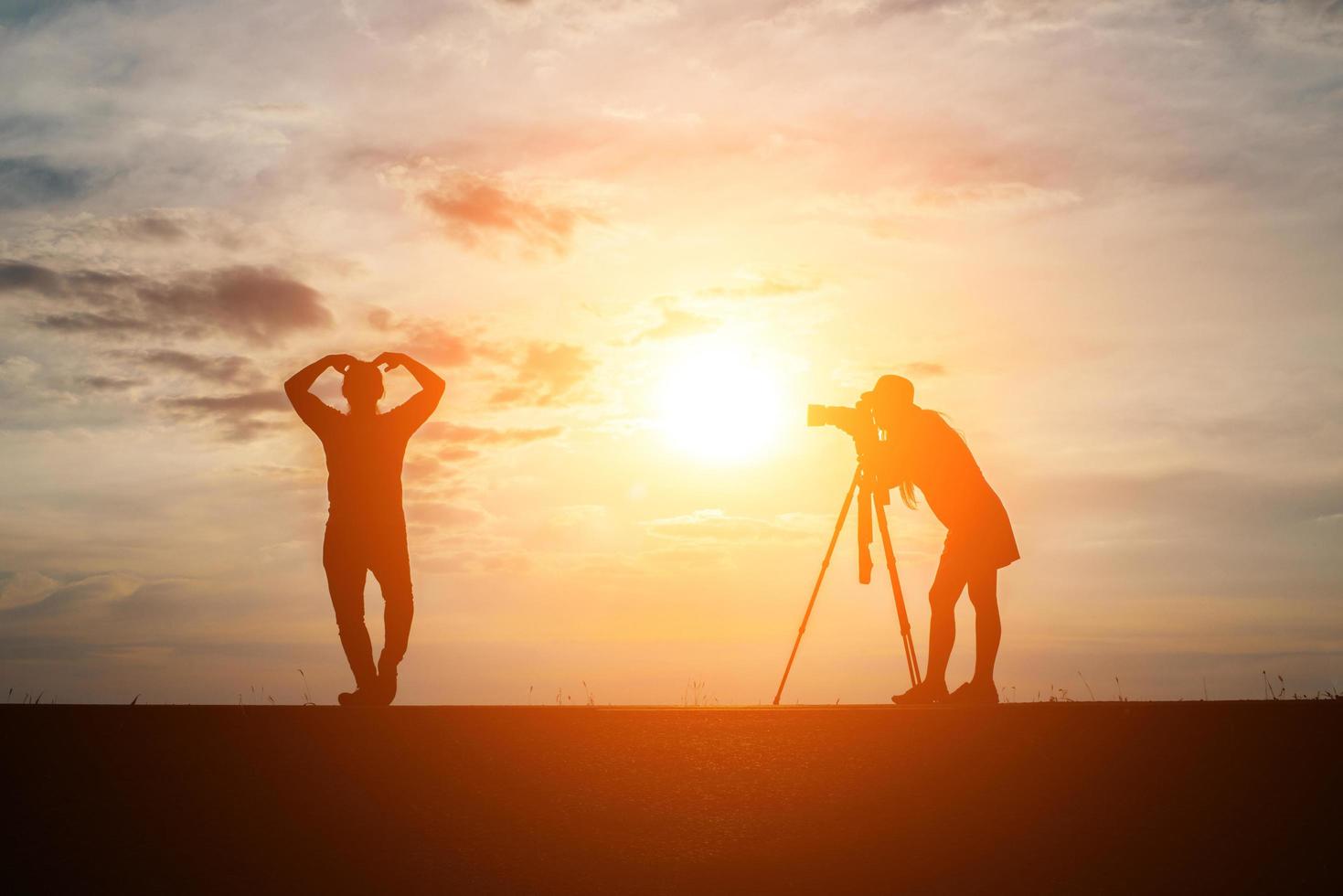 Silhouette eines Fotografen mit Modell und Kamera bei Sonnenuntergang foto