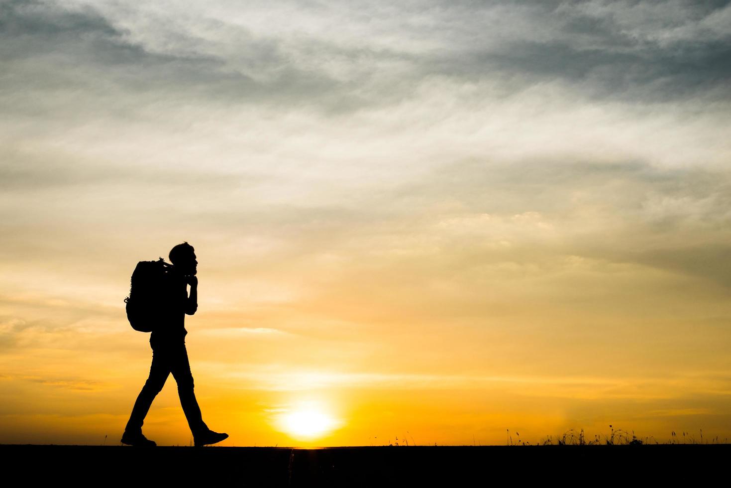 Schattenbild eines jungen Rucksacktouristenmannes, der während des Sonnenuntergangs geht foto