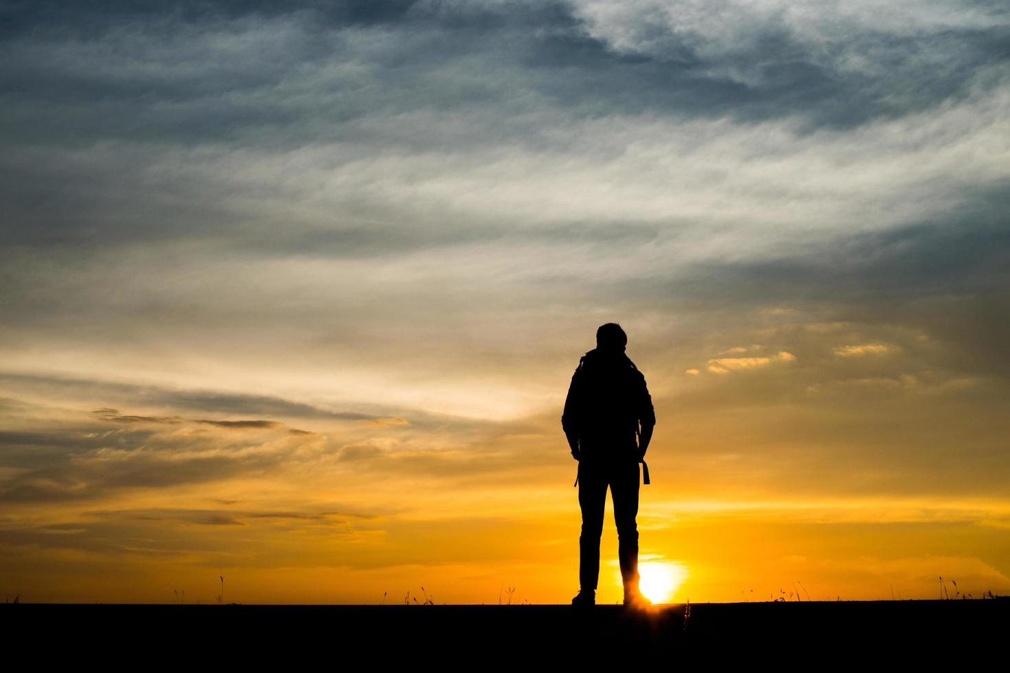 Schattenbild eines jungen Rucksacktouristenmannes, der während des Sonnenuntergangs geht foto
