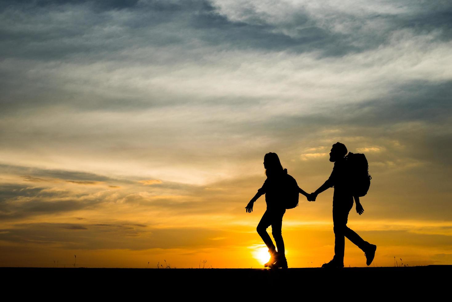 Silhouetten von zwei Wanderern mit Rucksäcken, die den Sonnenuntergang genießen foto