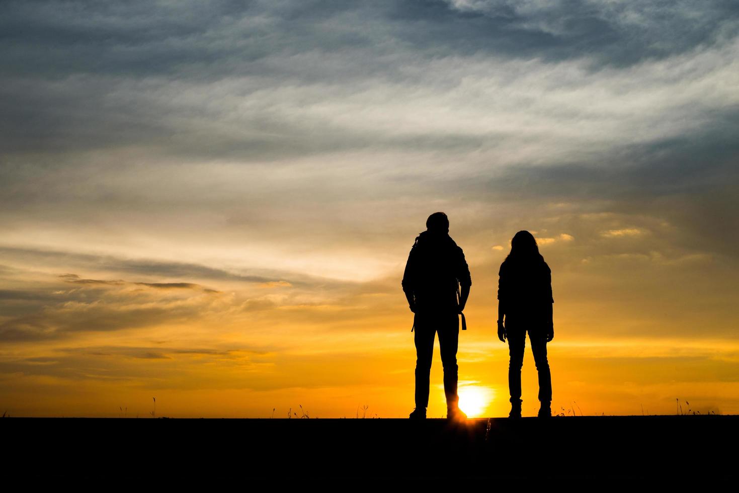 Silhouetten von zwei Wanderern mit Rucksäcken, die den Sonnenuntergang genießen foto