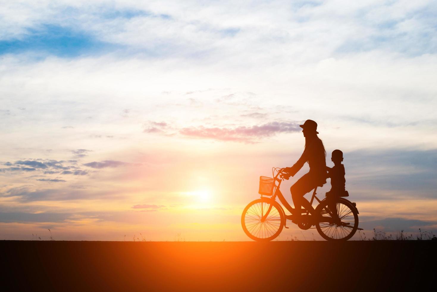 Mutter mit ihrem Kind Fahrrad fahren bei Sonnenuntergang foto