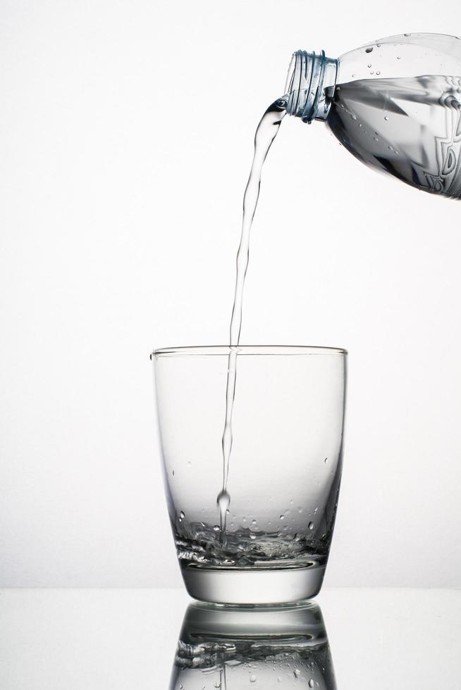 Nahaufnahme des gießenden Wasserspritzens im Glas lokalisiert auf weißem Hintergrund foto