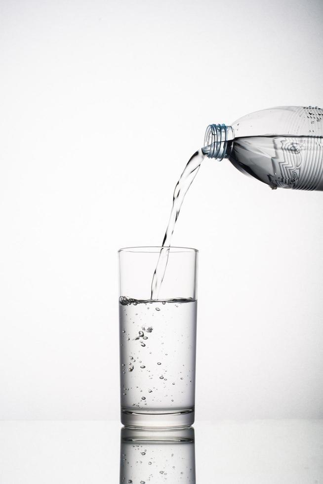 Nahaufnahme des gießenden Wasserspritzens im Glas lokalisiert auf weißem Hintergrund foto