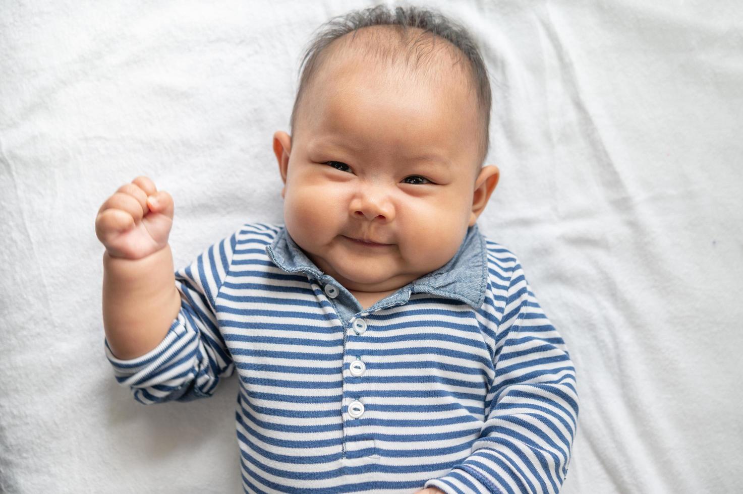 Baby, das Gesicht oben auf einem weißen Bett liegt und Kamera betrachtet foto