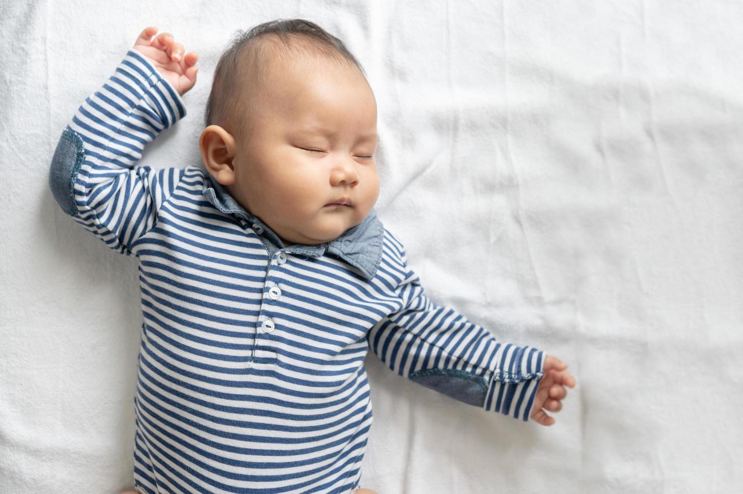 ein kleiner Junge in einem gestreiften Hemd, der im Bett schläft foto