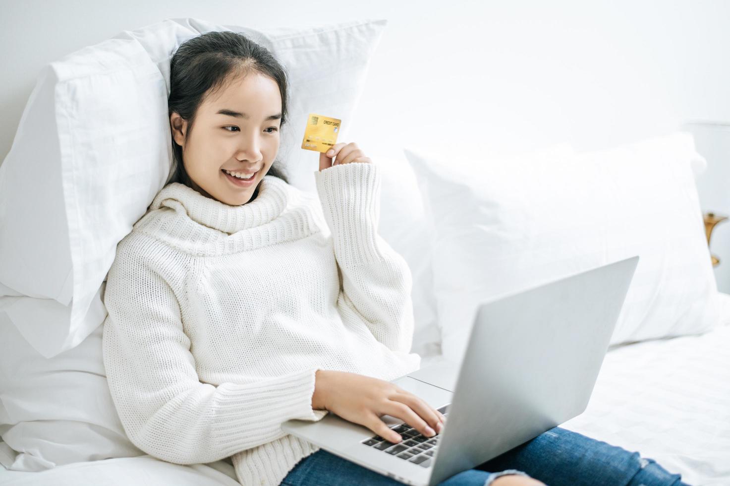 junge Frau, die auf Laptop einkauft und eine Kreditkarte hält foto