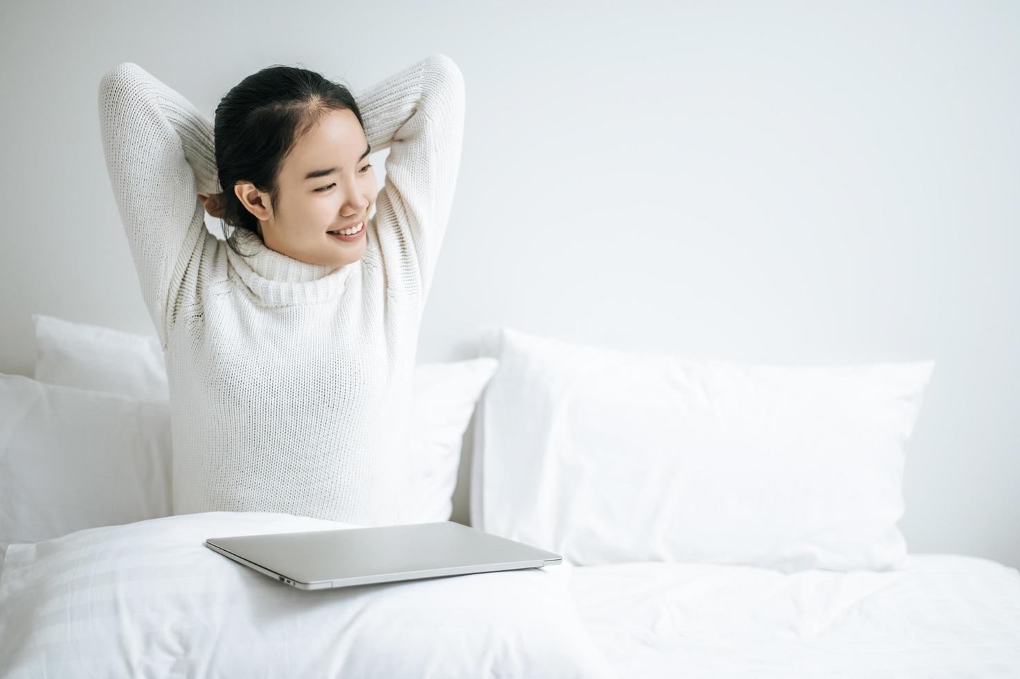 junge Frau, die auf Bett mit Laptop streckt foto