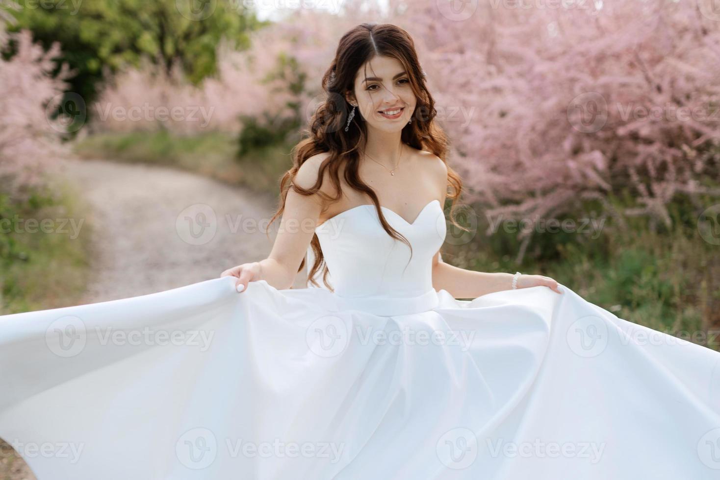 Eine junge Mädchenbraut in einem weißen Kleid dreht sich auf einem Weg foto
