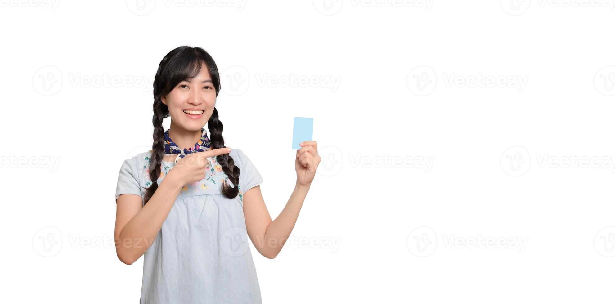 Portrait der schönen glücklichen jungen asiatischen Frau im Denimkleid, das Kreditkarte auf weißem Hintergrund hält foto