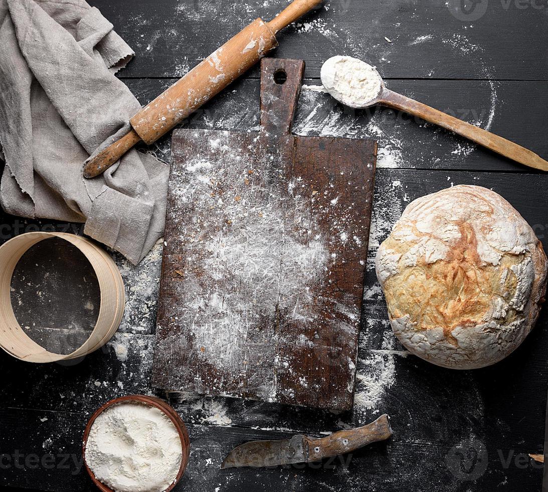 gebackenes Brot, weißes Weizenmehl, hölzernes Nudelholz und altes Schneidebrett foto