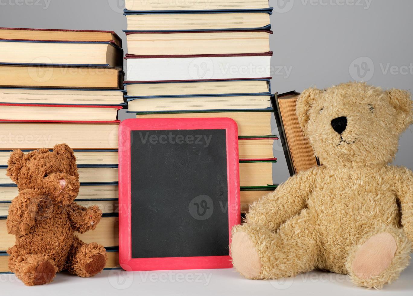 Teddybär und leeres schwarzes Brett im roten Rahmen auf dem Hintergrund des Bücherstapels foto