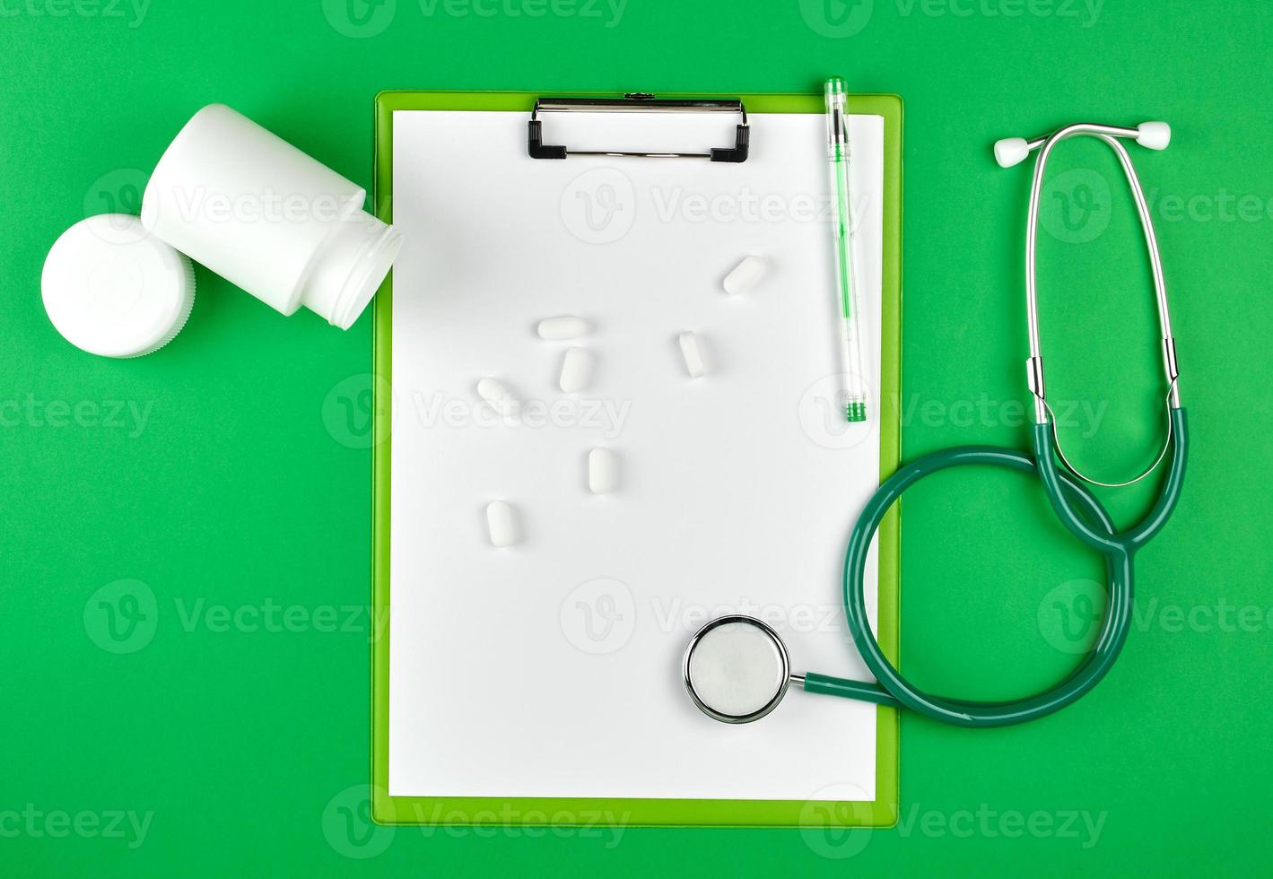 verstreute weiße ovale tabletten aus einem plastikglas, stethoskop foto