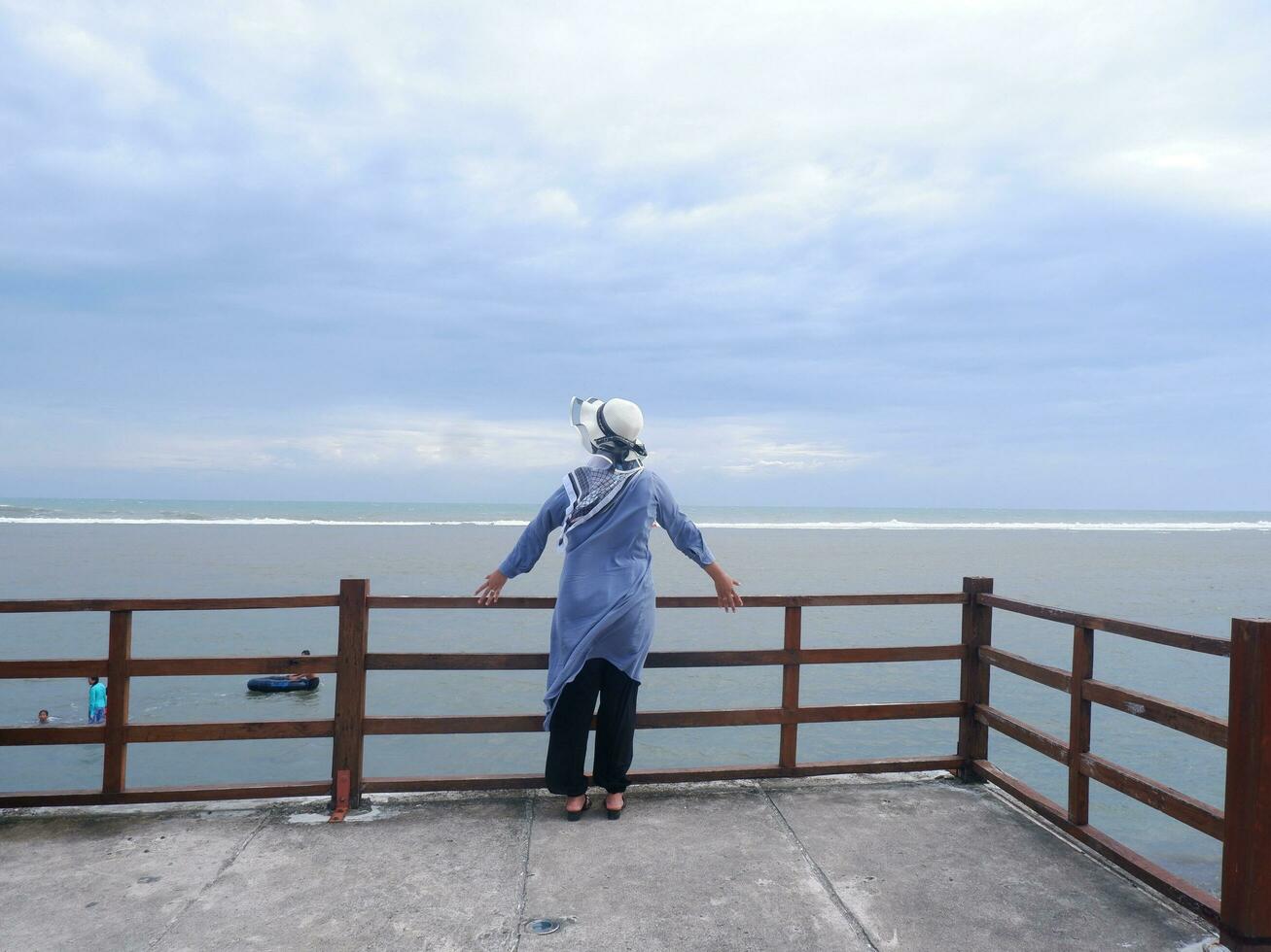 Rücken der Frau mit Hut am tropischen Strand, die von der Brücke aus auf den Himmel und das Meer blickte. Seeblick foto