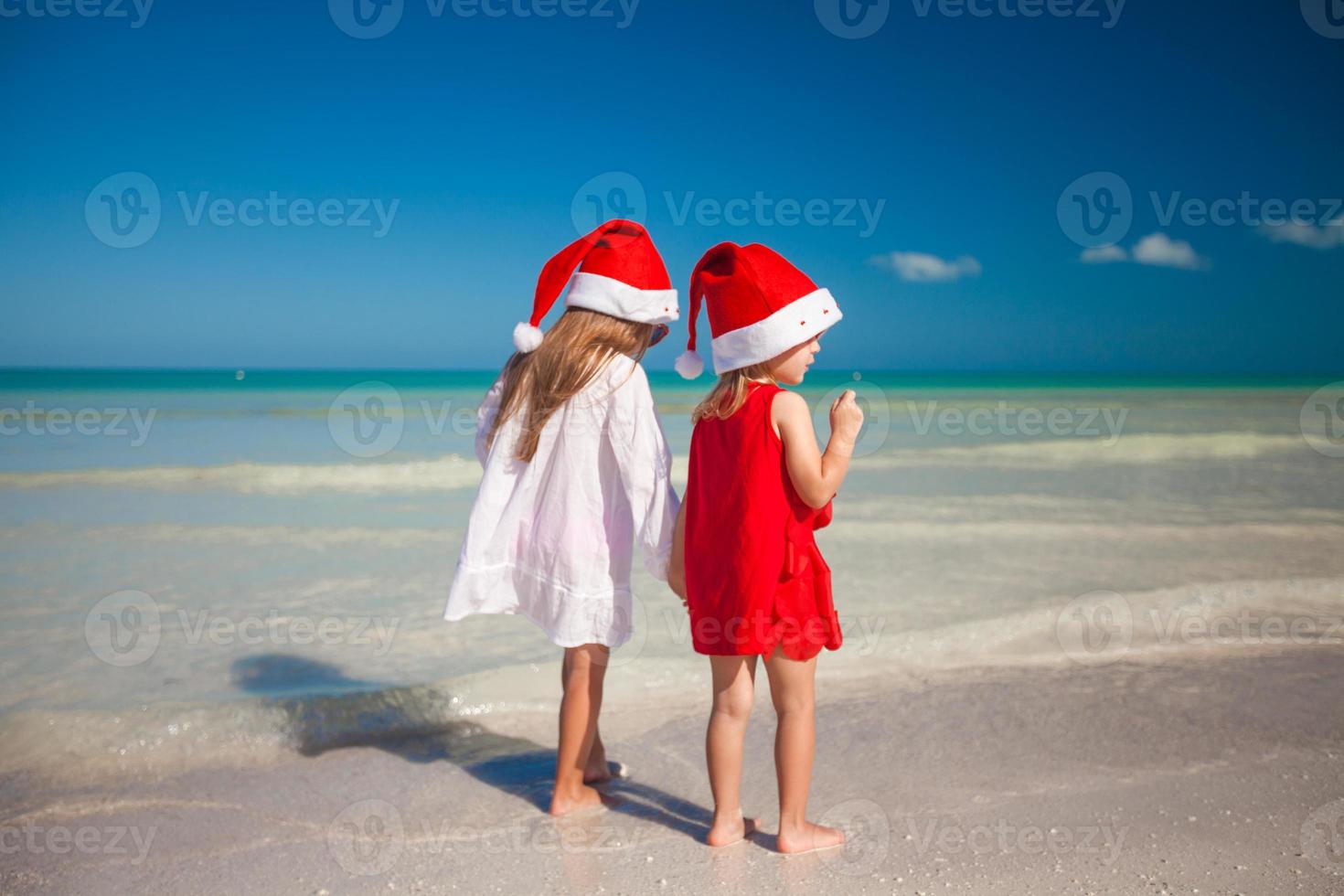 Rückansicht von kleinen süßen Mädchen in Weihnachtsmützen am exotischen Strand foto