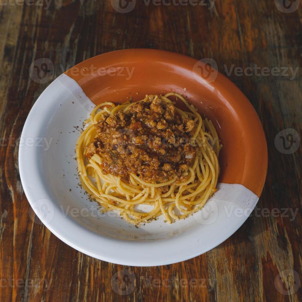 gesunder Teller italienischer Spaghetti mit einer leckeren Bolognese-Sauce aus Tomaten und Rinderhackfleisch und frischem Basilikum auf einem rustikalen braunen Holztisch foto