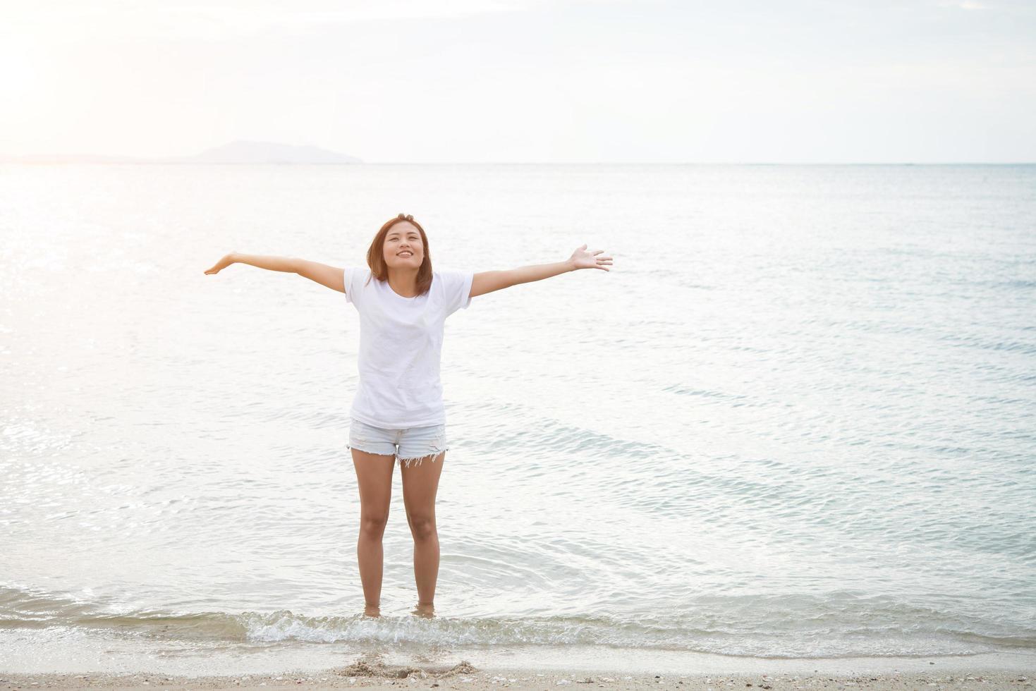 junge schöne Frau streckt ihre Arme in der Luft am Strand mit bloßen Füßen foto
