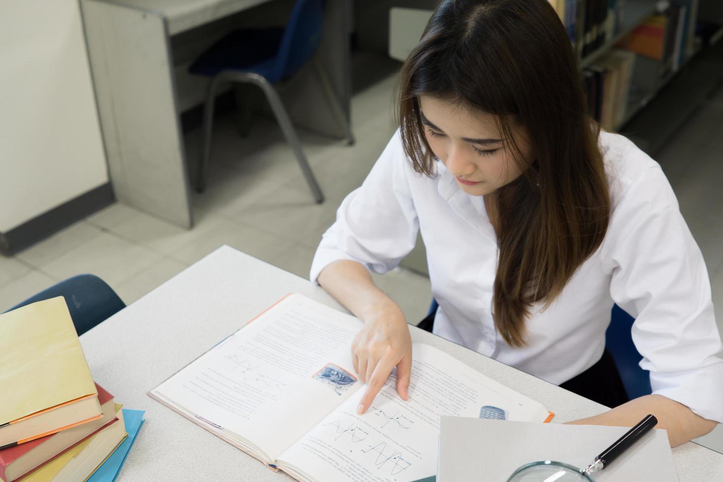 junger asiatischer Student, der in der Bibliothek liest foto