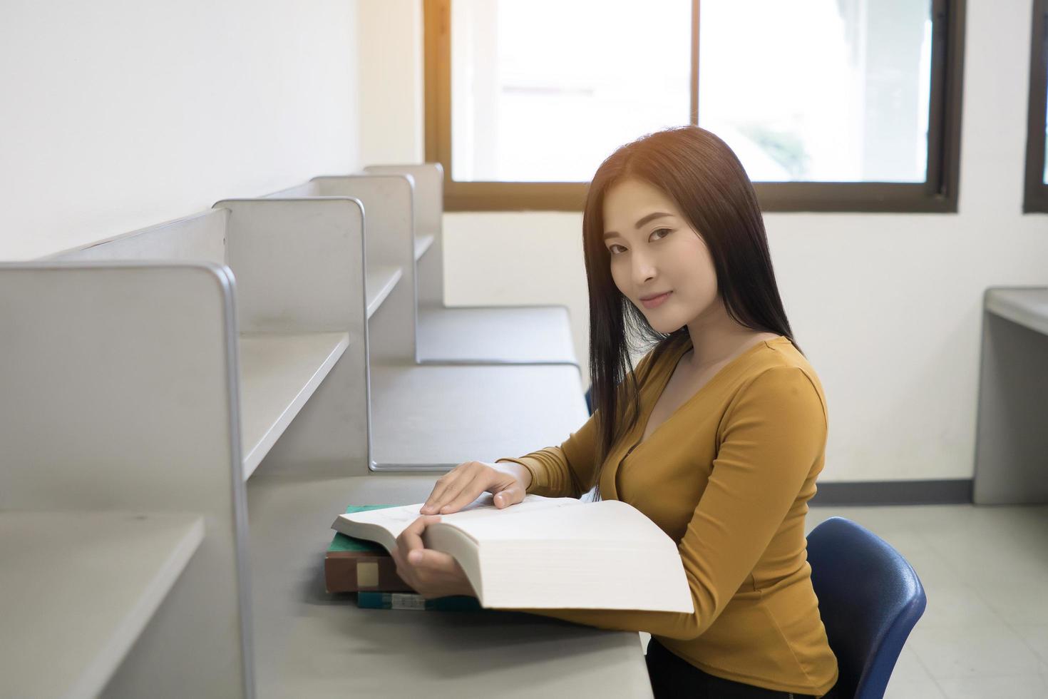 junger asiatischer Student, der in der Bibliothek liest foto