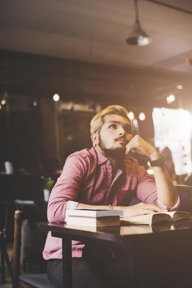 junger bärtiger Hipster, der ein Buch in einem Café liest foto